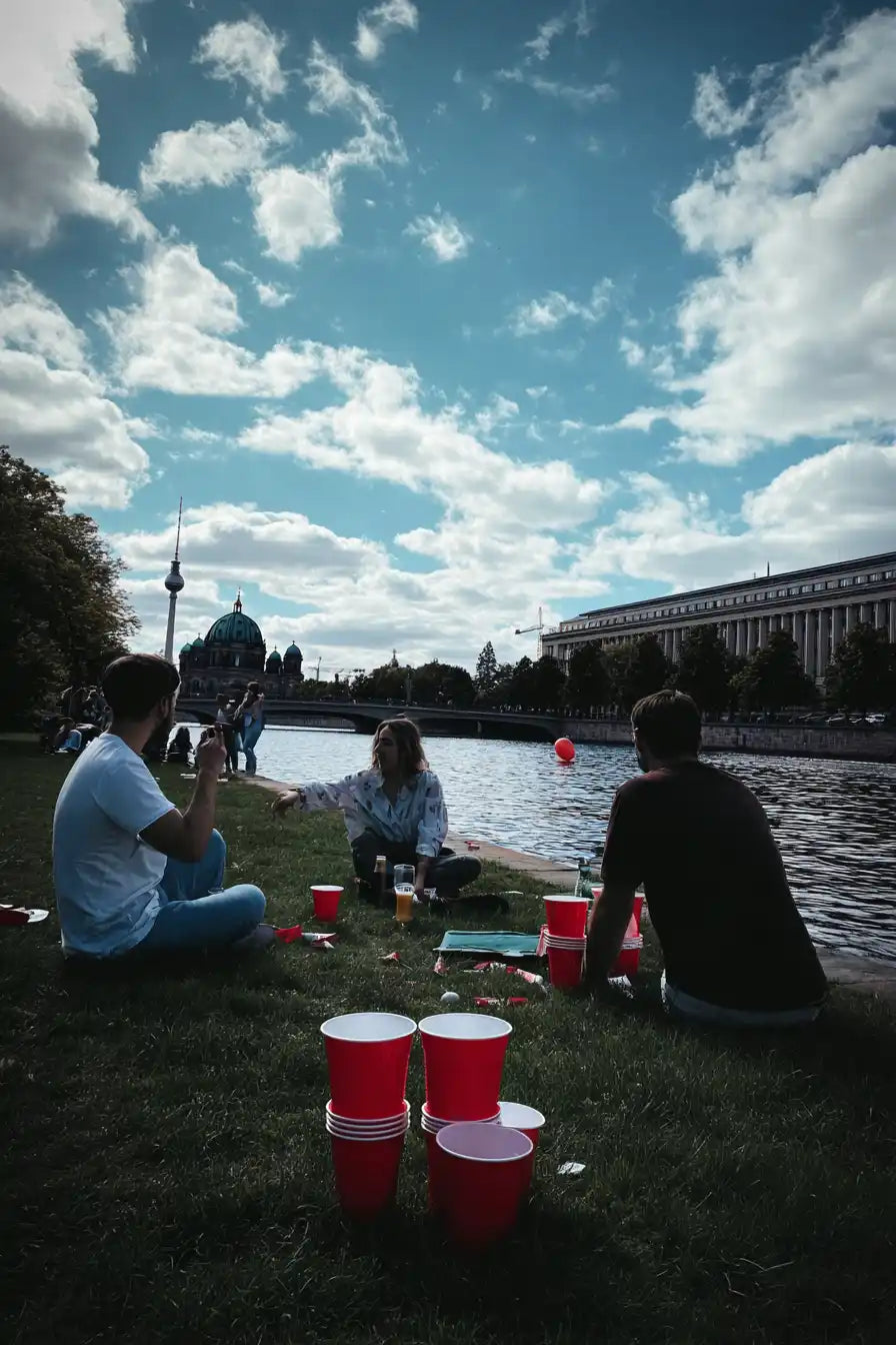 Eine Gruppe von Menschen sitzt auf Gras am Fluss mit roten Plastikbechern.